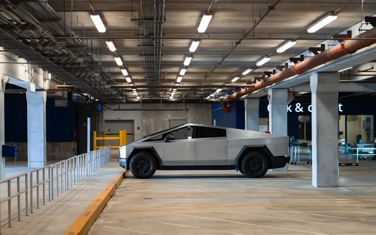 An electric Cybertruck is parked in a modern underground garage, showcasing futuristic automotive design.