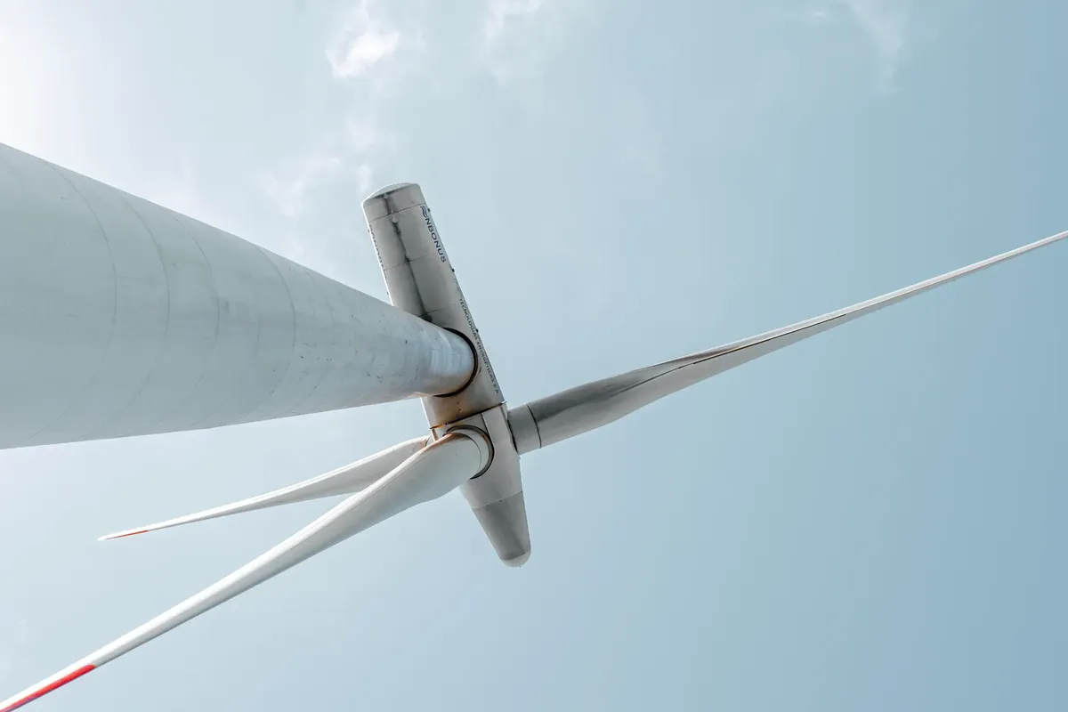 Looking up at a majestic wind turbine under a clear blue sky, showcasing renewable energy innovation.