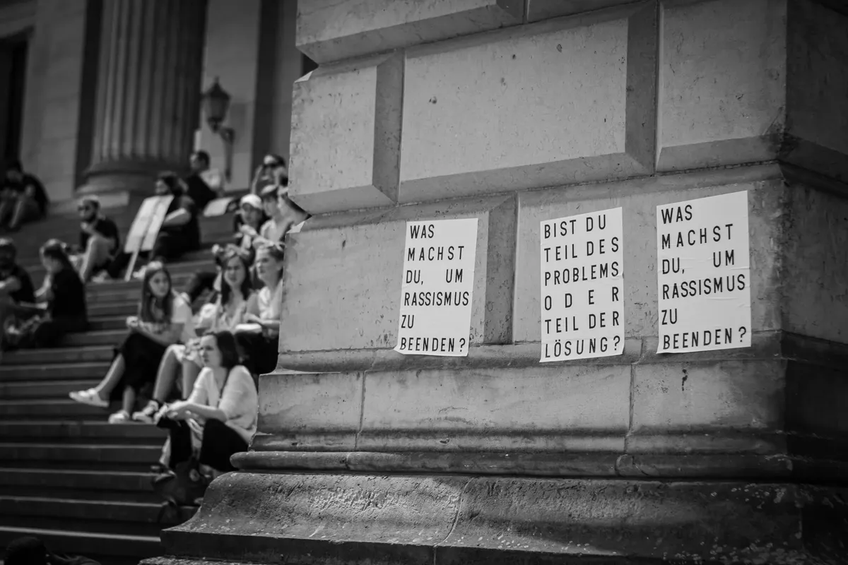 Protesters gather in Berlin, Germany, with anti-racism messages displayed, captured in black and white.